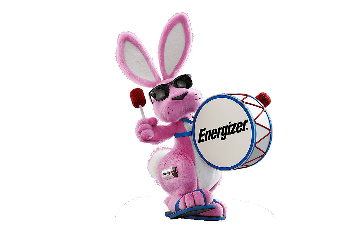 The Energizer Bunny mascot wearing large, rectangular framed black sunglasses, blue sandals and using two drum sticks with red ends to bang a drum featuring the Energizer logo and resting on the Bunny’s belly by being supported by two blue shoulder straps